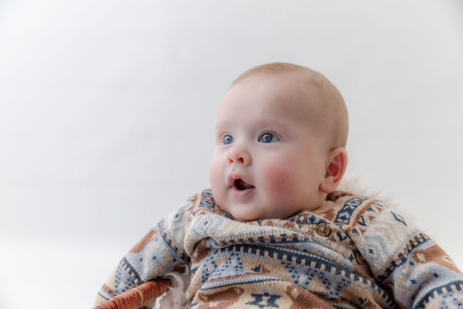 A baby wearing a cozy Fair Isle patterned sweater looks up with wonder against a white background.