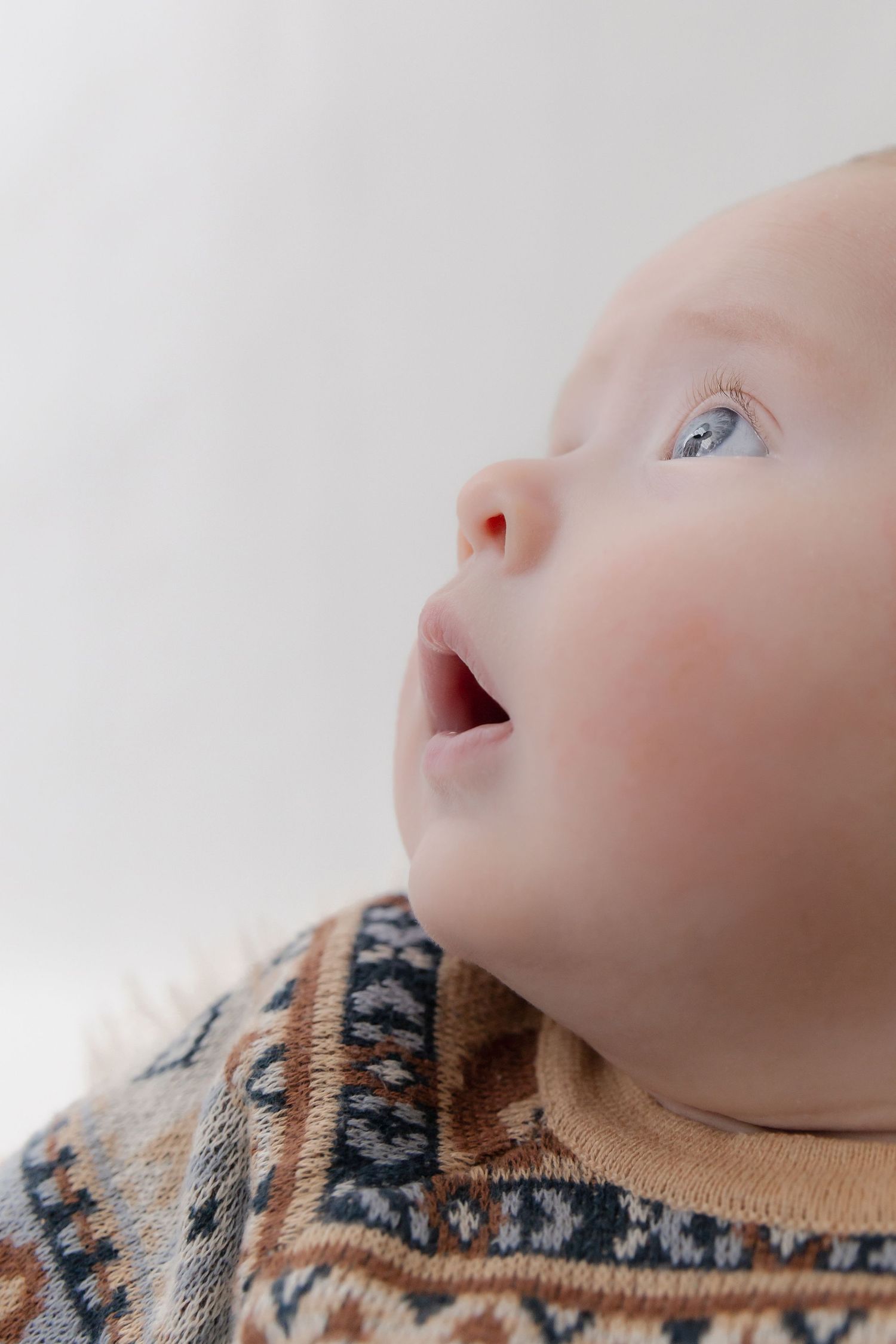 Close-up view of an infant wearing a patterned knit sweater looking upward with wonder against a light background.