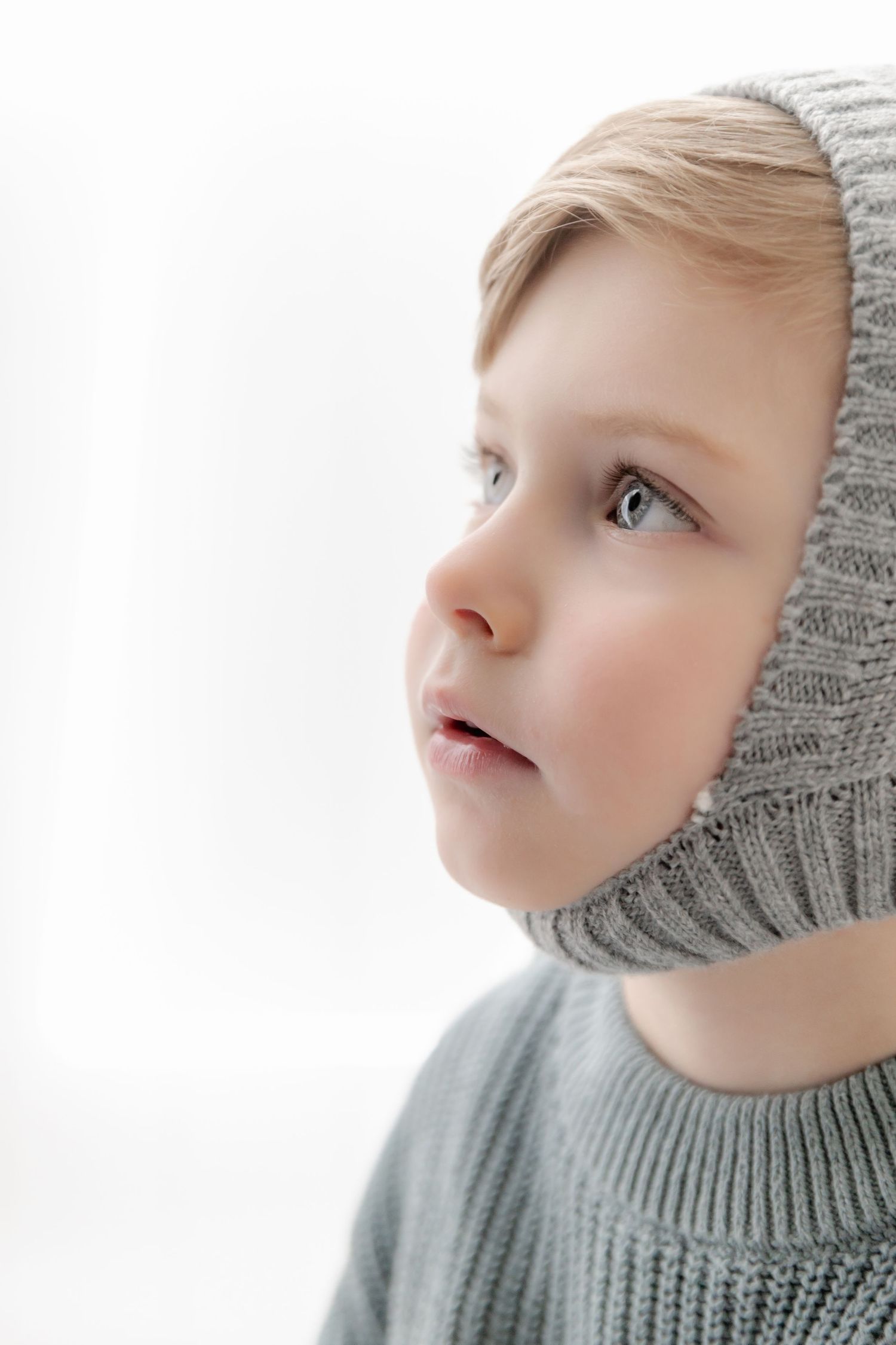 Close-up profile view of a young child wearing a gray knit sweater gazing upward with a thoughtful expression.
