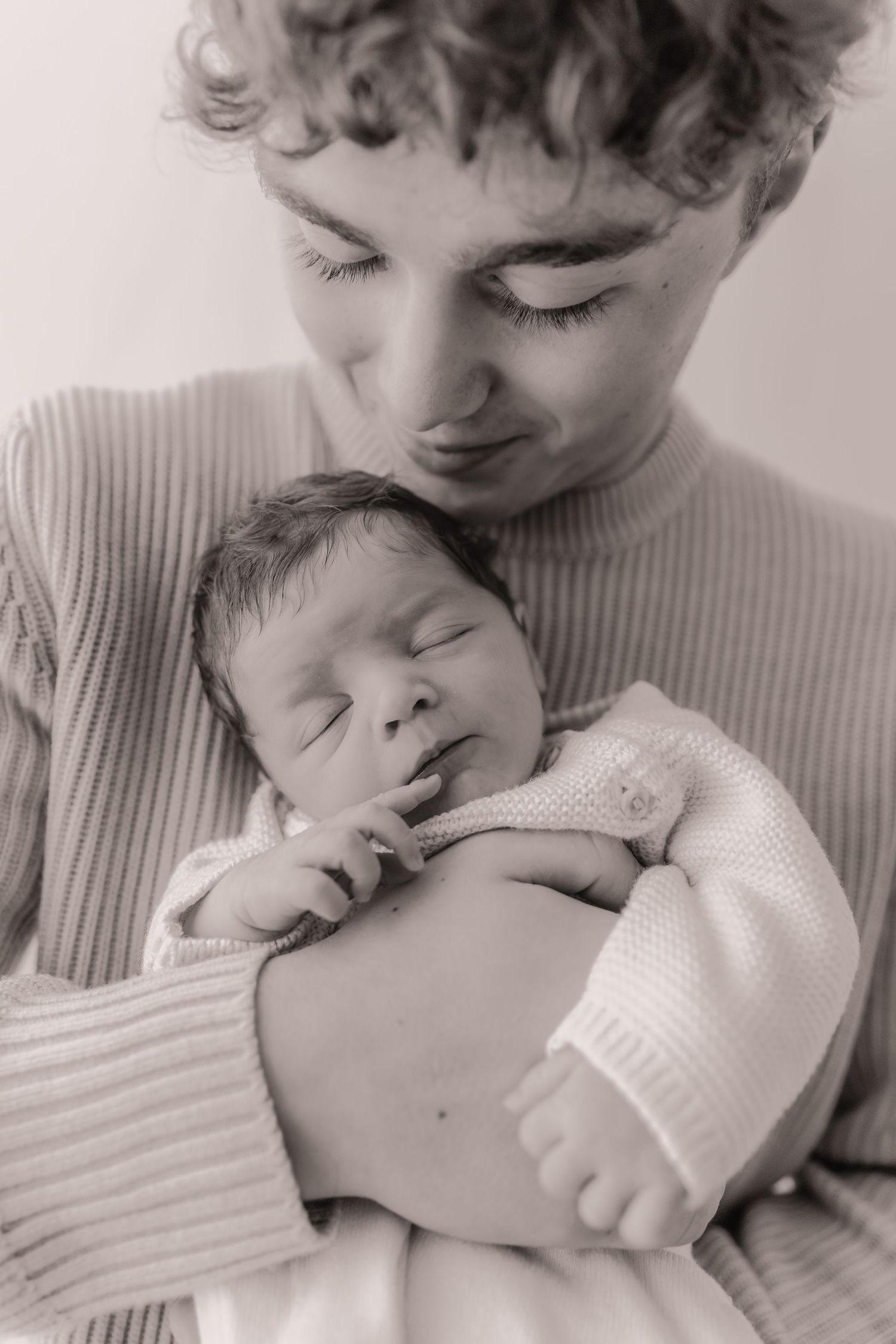 Black and white photo series showing tender moments between siblings as an older child gently embraces a sleeping baby.
