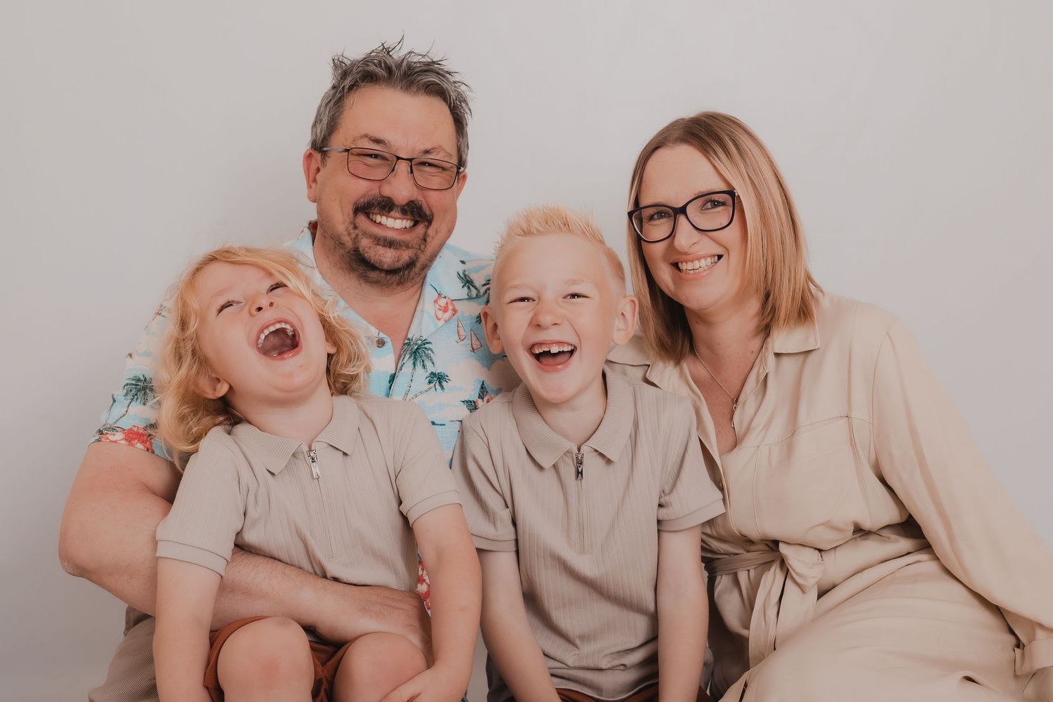 Family members wearing coordinated neutral tones pose playfully on a light background. Photographer. Hull. East Yorkshire. Photography