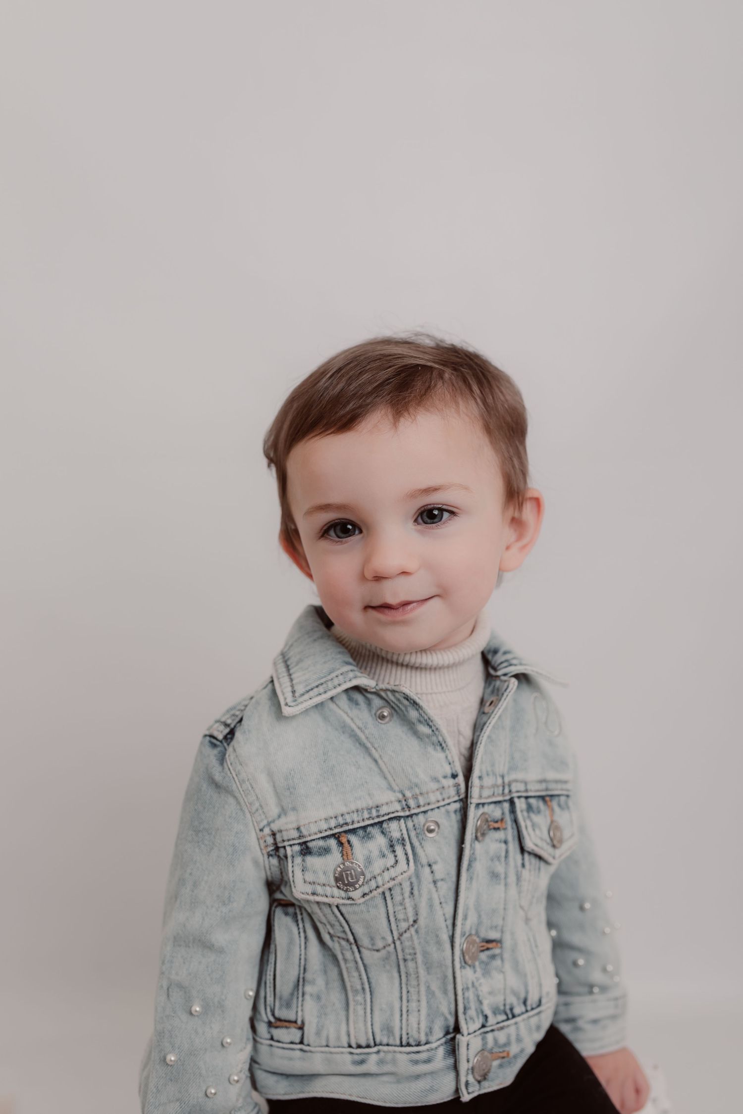 Young child wearing light denim jacket poses against neutral grey background in studio. Photographer. Hull. East Yorkshire. Photography