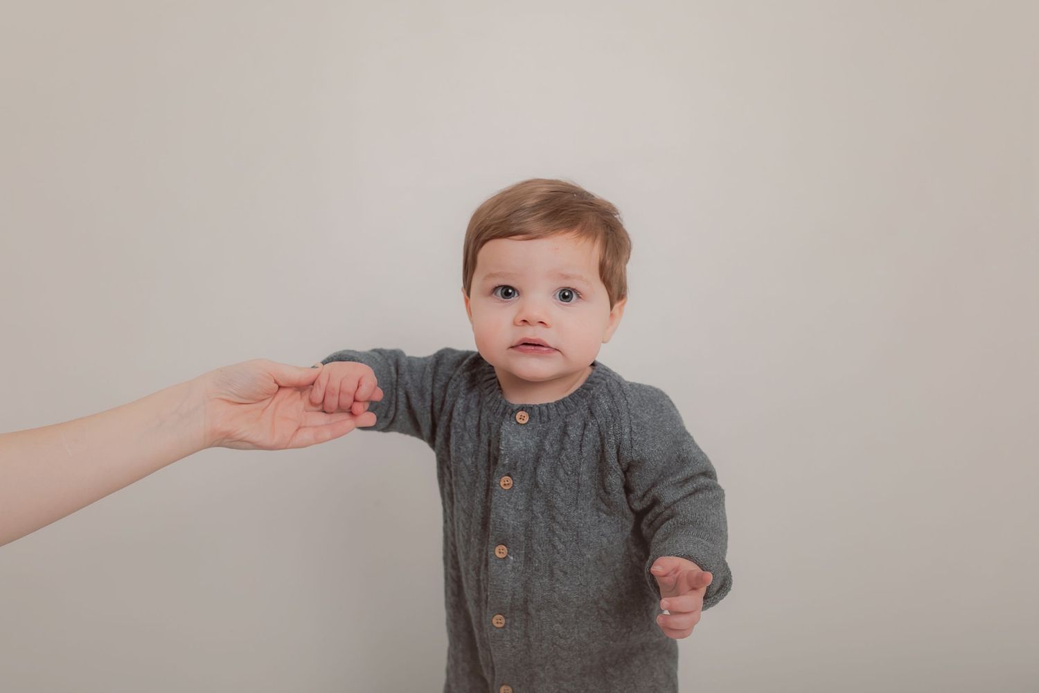 A toddler in a grey knit romper holding an adult's hand against a light background. Photographer. Hull. East Yorkshire. Photography