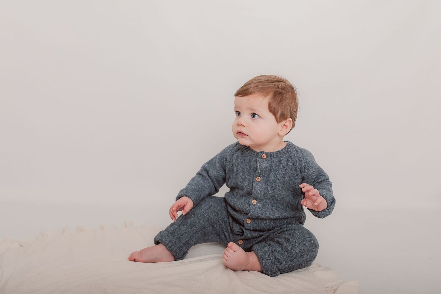A toddler in grey knitwear sitting on a light colored floor during a photo session. Photographer. Hull. East Yorkshire. Photography