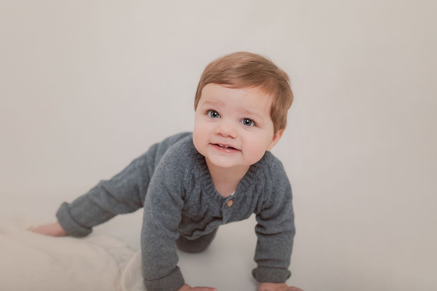 A toddler in grey clothing crawling on a white surface during a studio photoshoot. Photographer. Hull. East Yorkshire. Photography