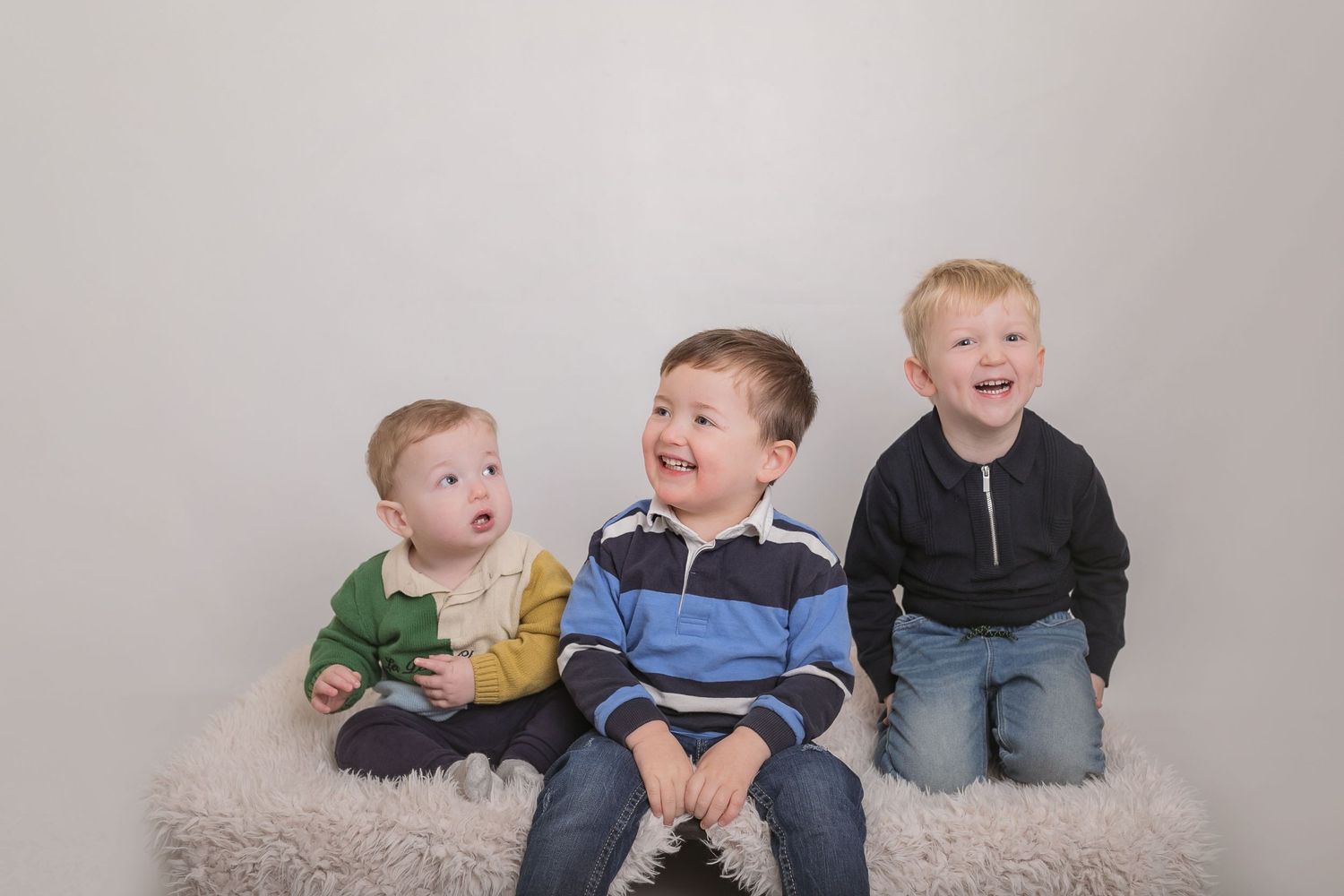 Three children share laughter while sitting together on a grey backdrop. Photographer. Hull. East Yorkshire. Photography