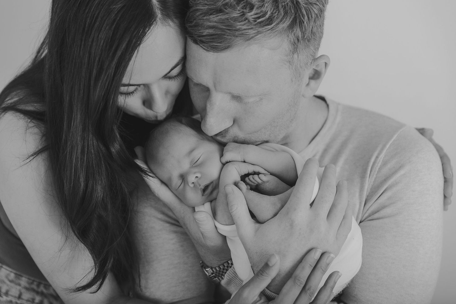 Black and white photo of parents cradling and kissing their newborn baby.  Photographer. Hull. East Yorkshire. Photography