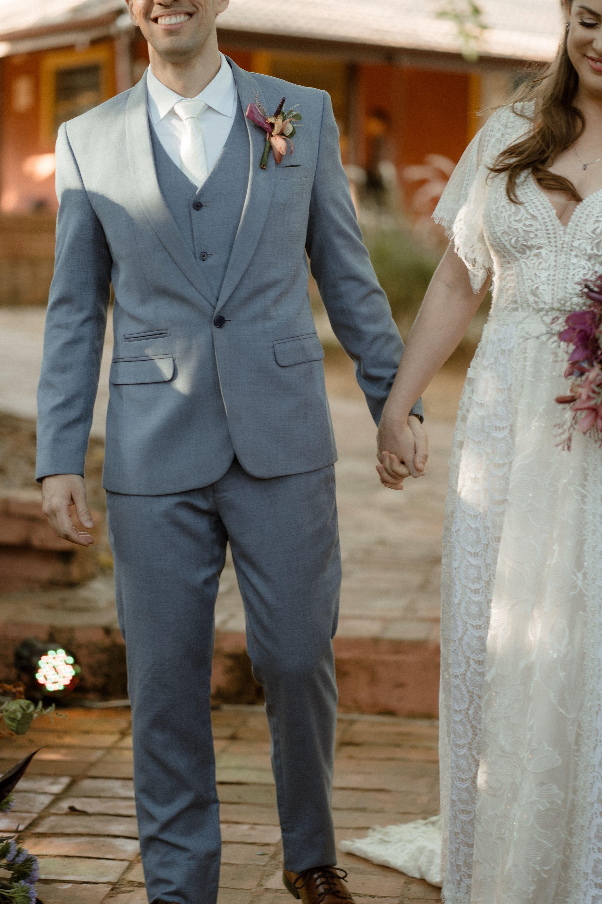 Wedding couple walking hand in hand on rustic brick pavement.