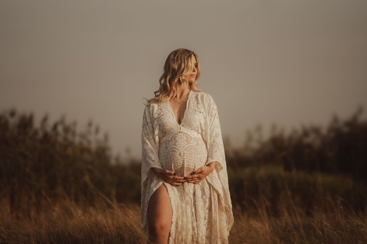 Close-up silhouette of hands gently touching a pregnant belly at sunset.