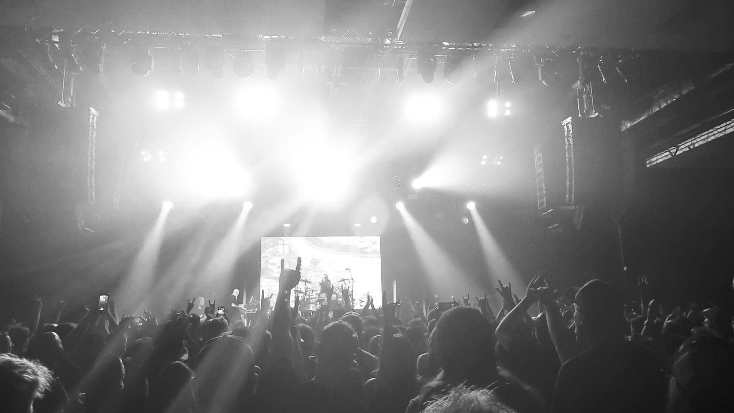 Enthusiastic audience with raised hands at outdoor event under colorful tents.