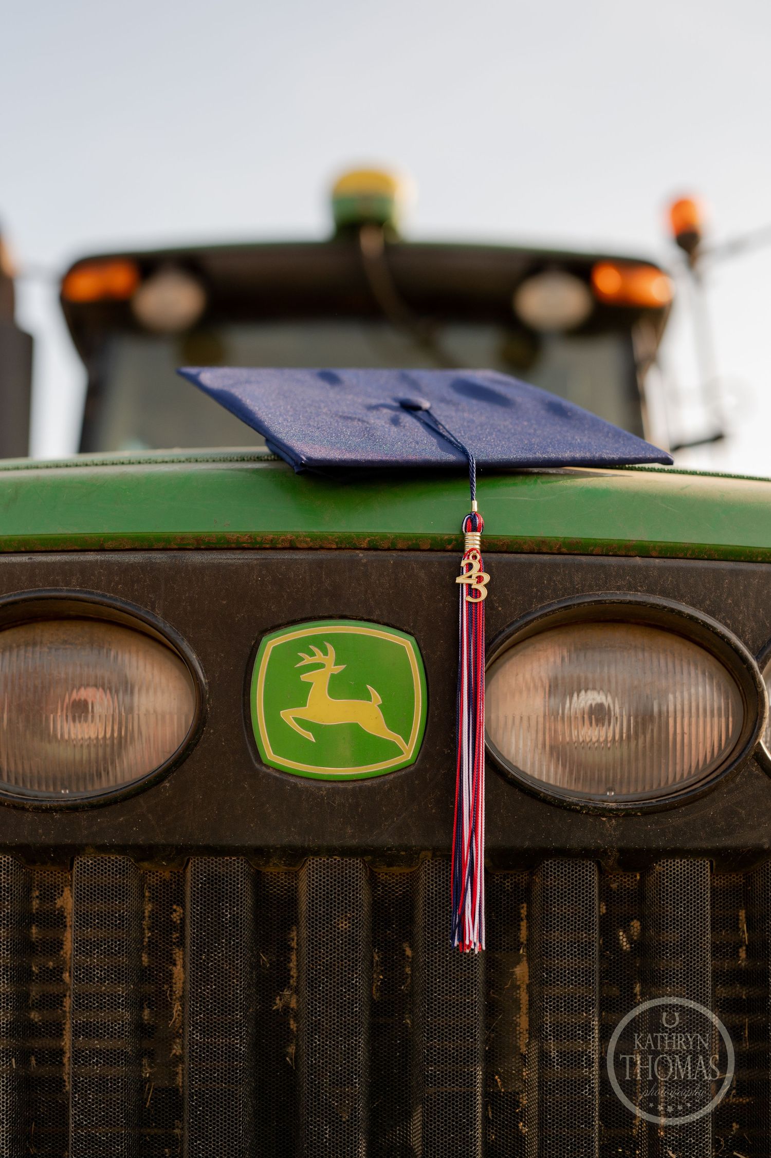 Graduation cap with tassel rests on John Deere tractor grill.