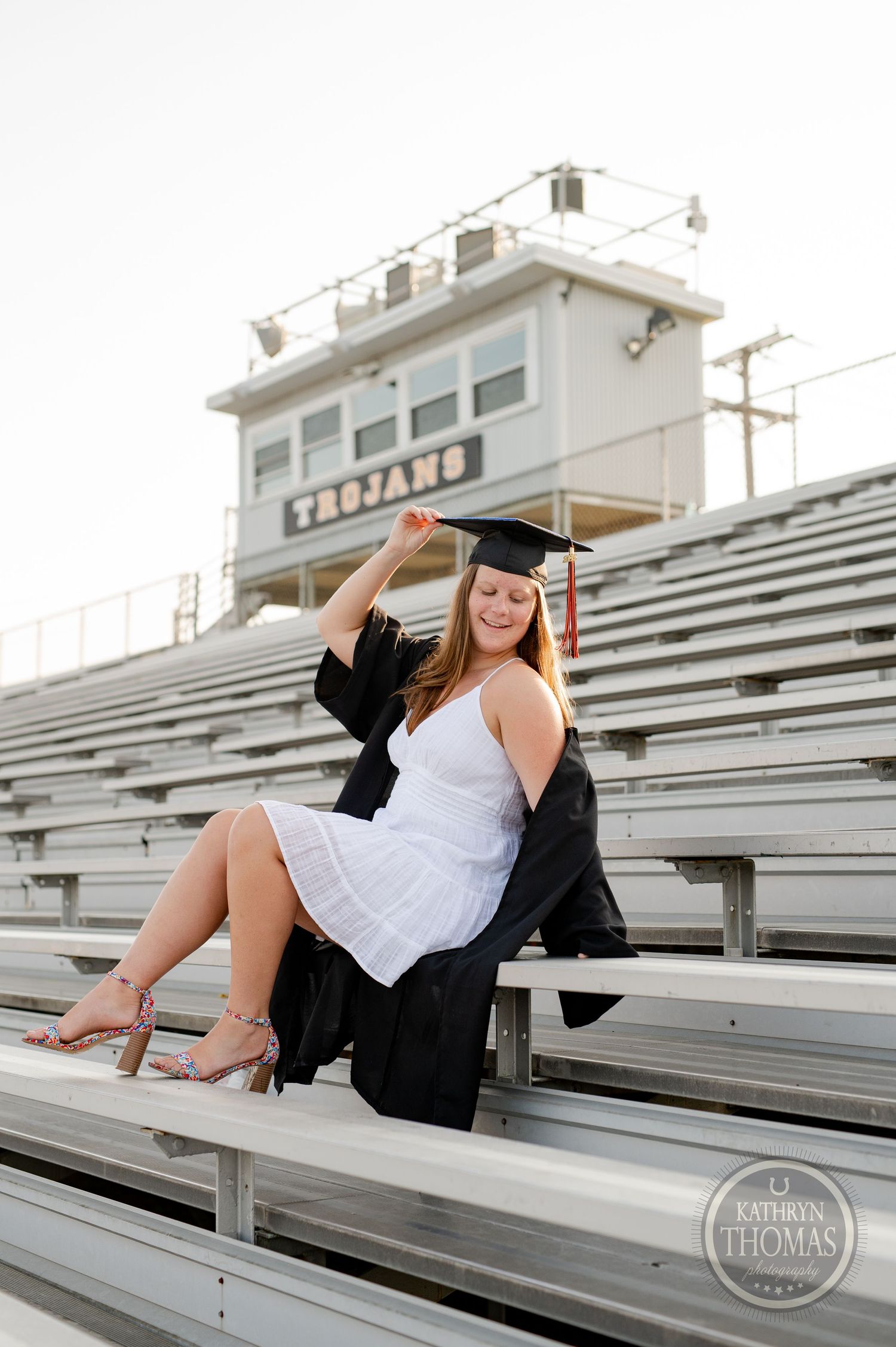 Graduation portrait on stadium bleachers with white press building behind.