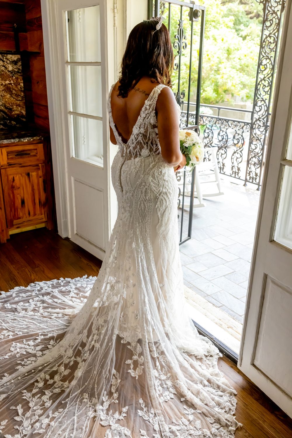 Wedding gown with intricate lace details and cathedral train photographed by French doors leading to balcony.