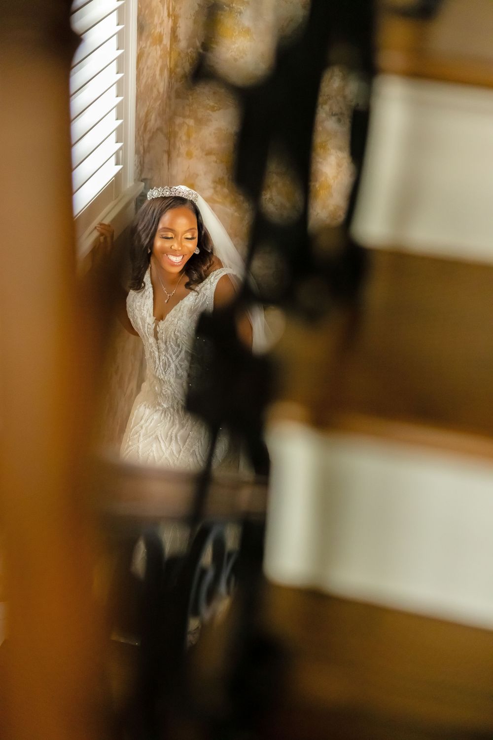 Ethereal bridal portrait through wooden architectural elements with soft bokeh effects.