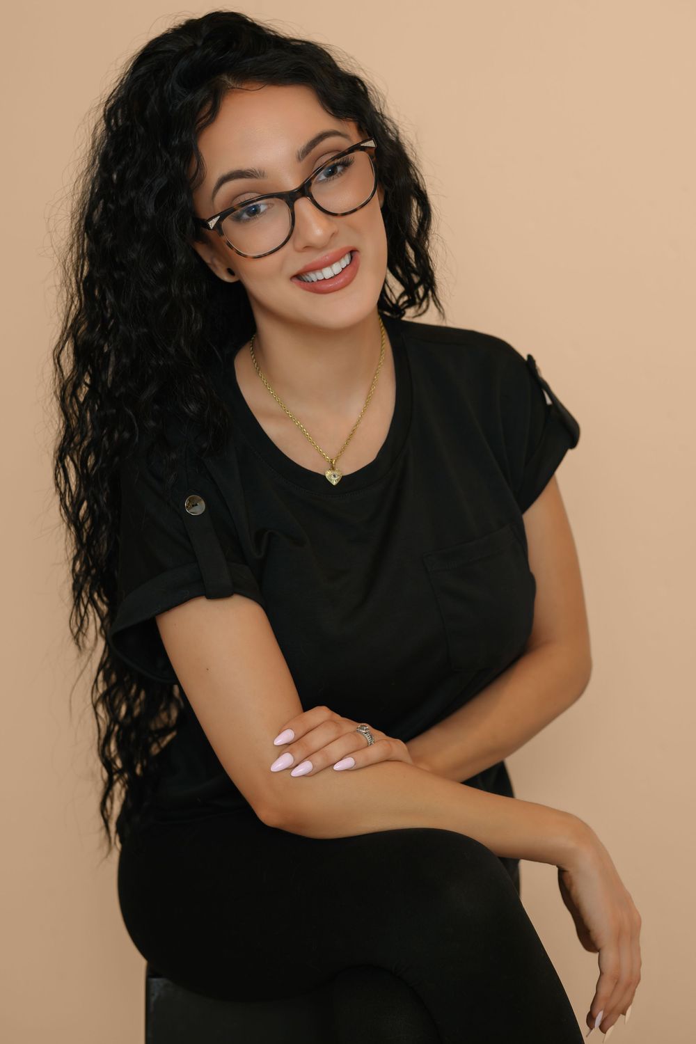 Professional portrait series of someone in a black top and glasses against a neutral beige background with natural lighting.