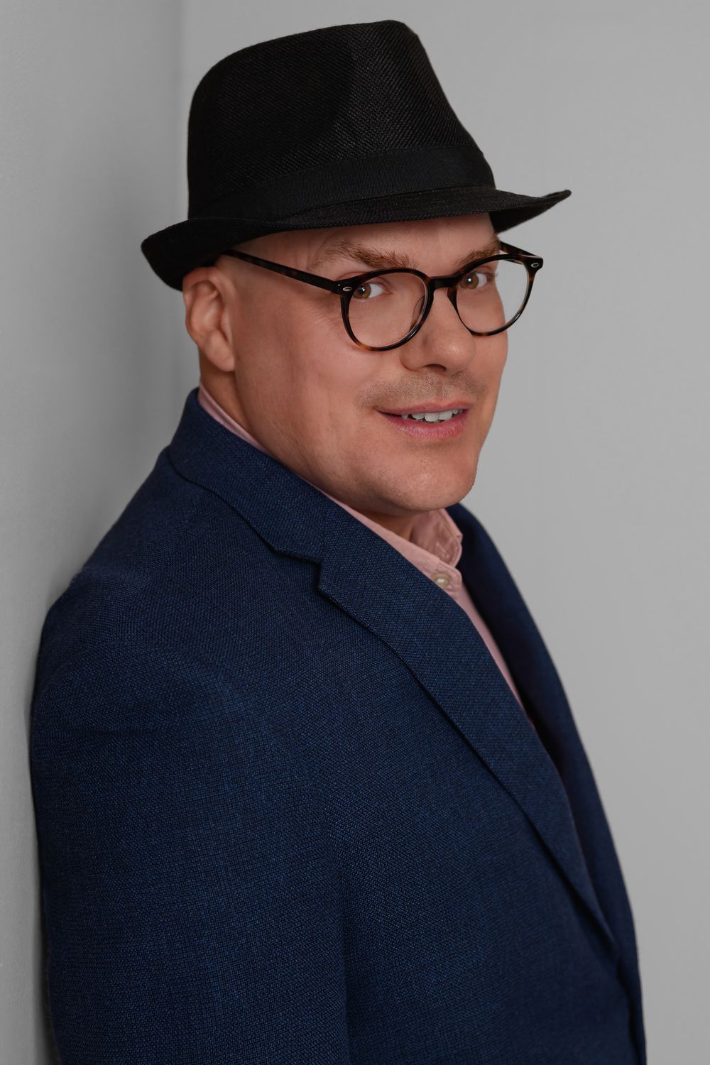 Professional headshot series showing person in navy blazer and black hat against gray background from different angles.