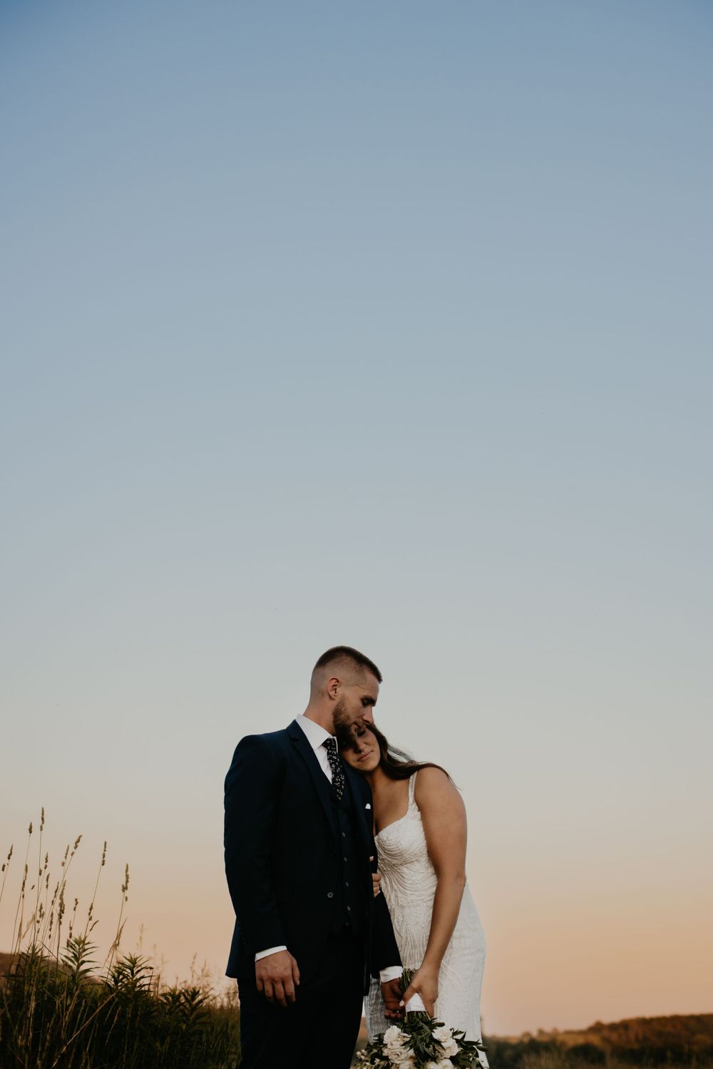 A romantic sunset portrait of newlyweds against a soft blue sky.