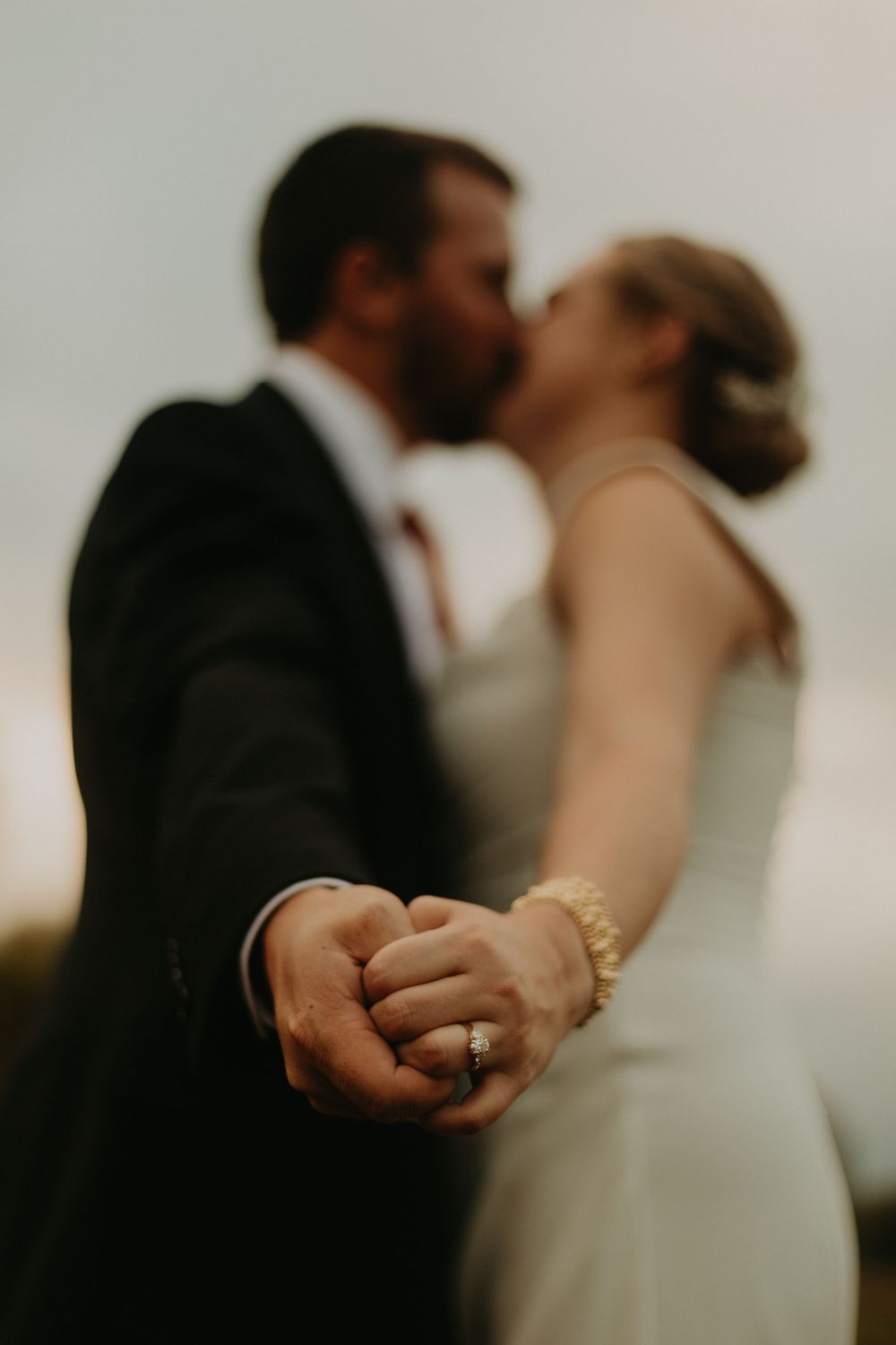 Close-up shot of wedding rings with couple embracing in soft focus background.