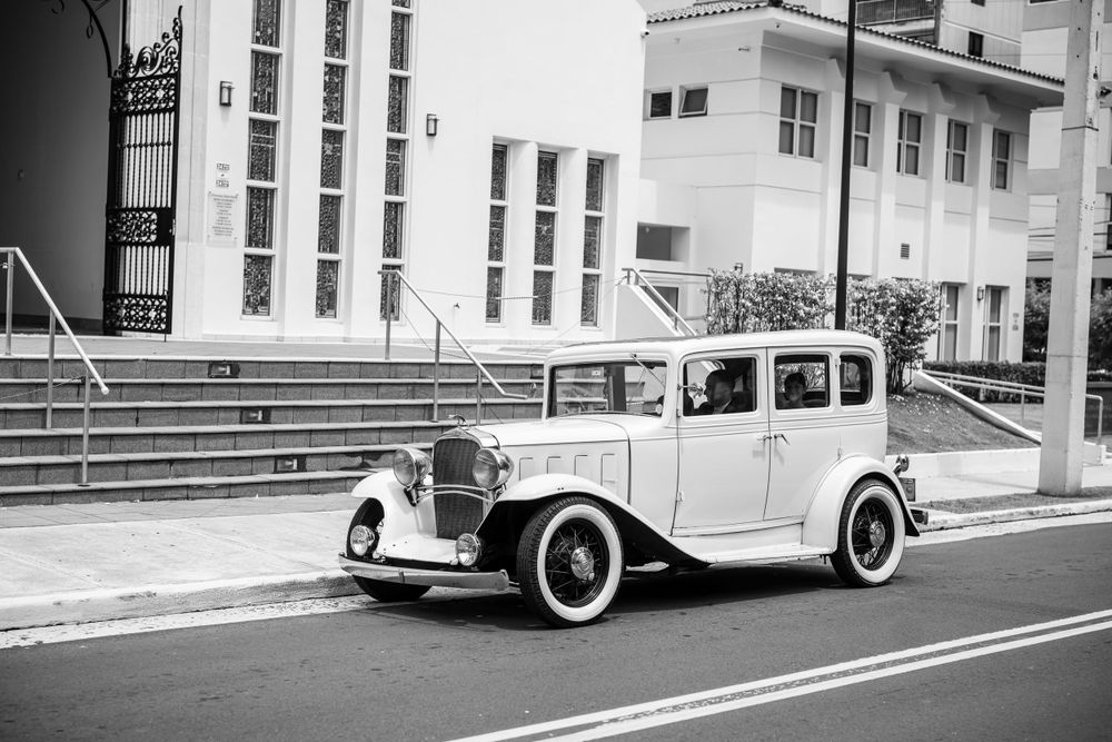 Vintage white Rolls Royce parked outside classic church building.
