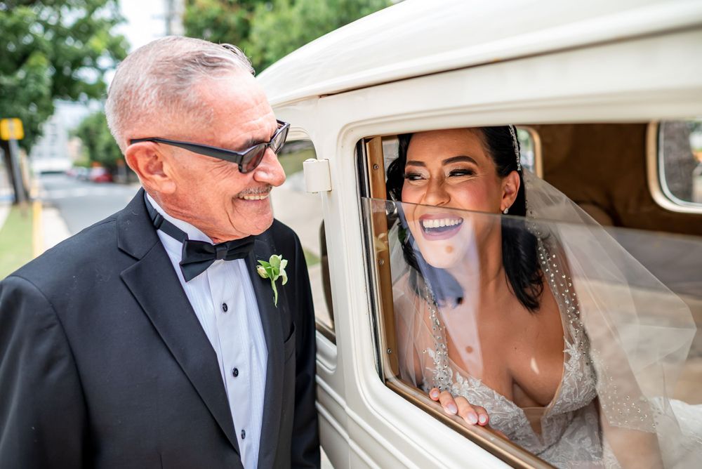 Joyful wedding moment captured beside vintage white car.