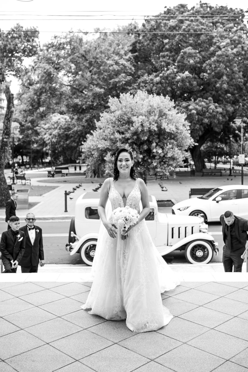 Black and white bridal portrait with vintage car in background.