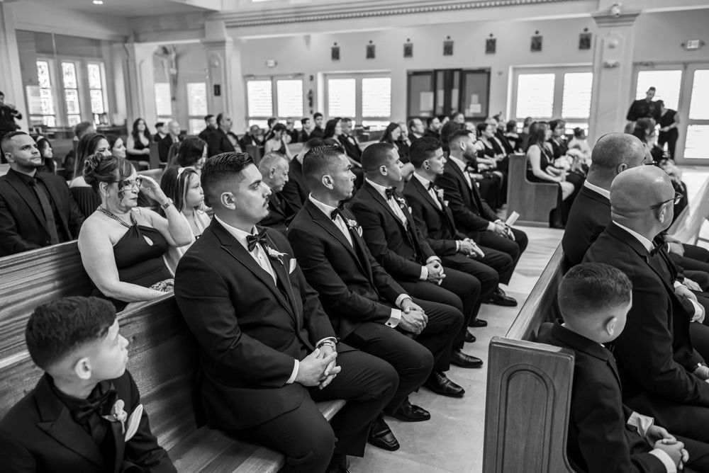Black and white photo of wedding guests seated in church pews during ceremony.
