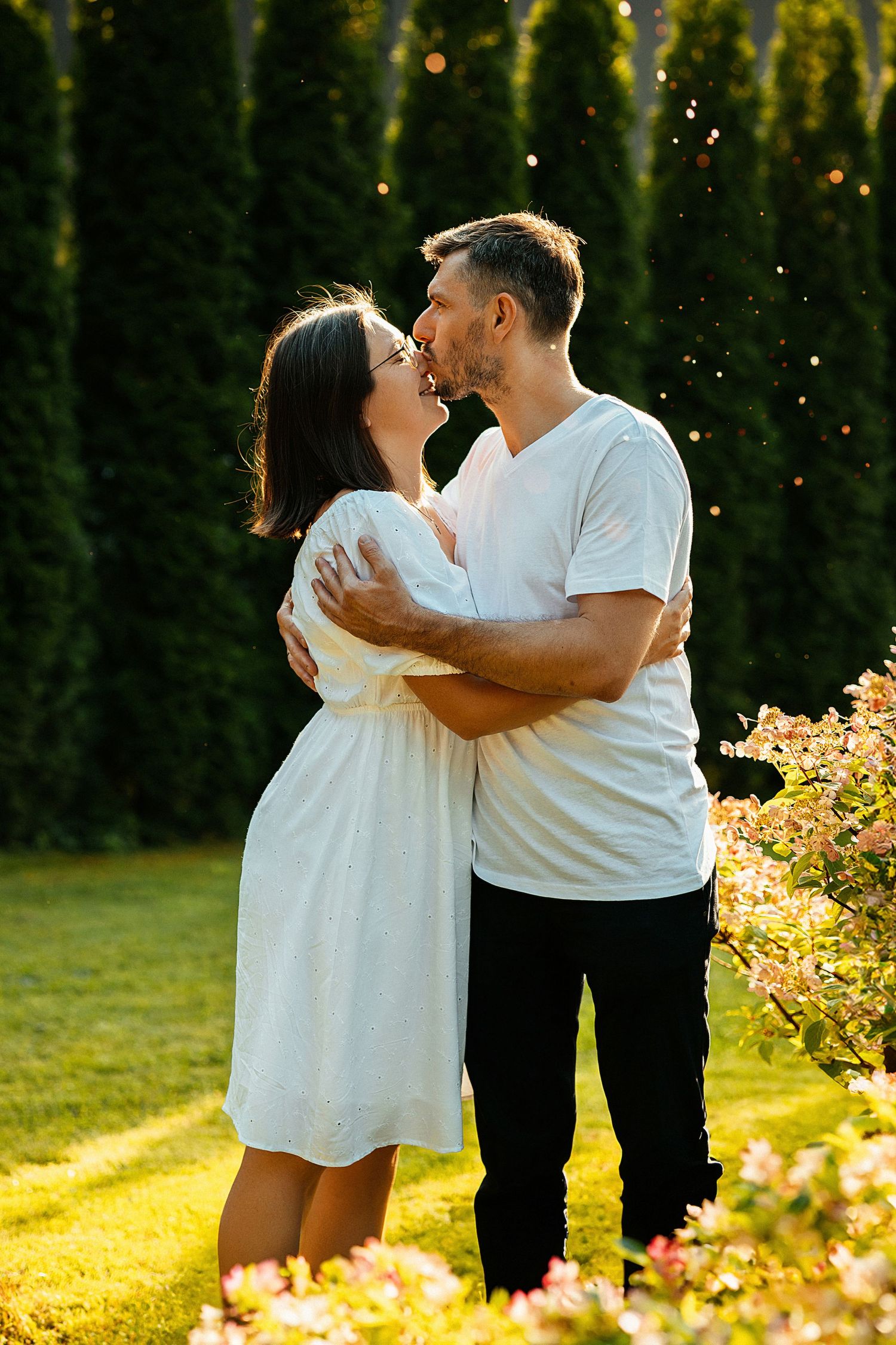 a man  in the setting sun hugs and kisses his wife  on the nose