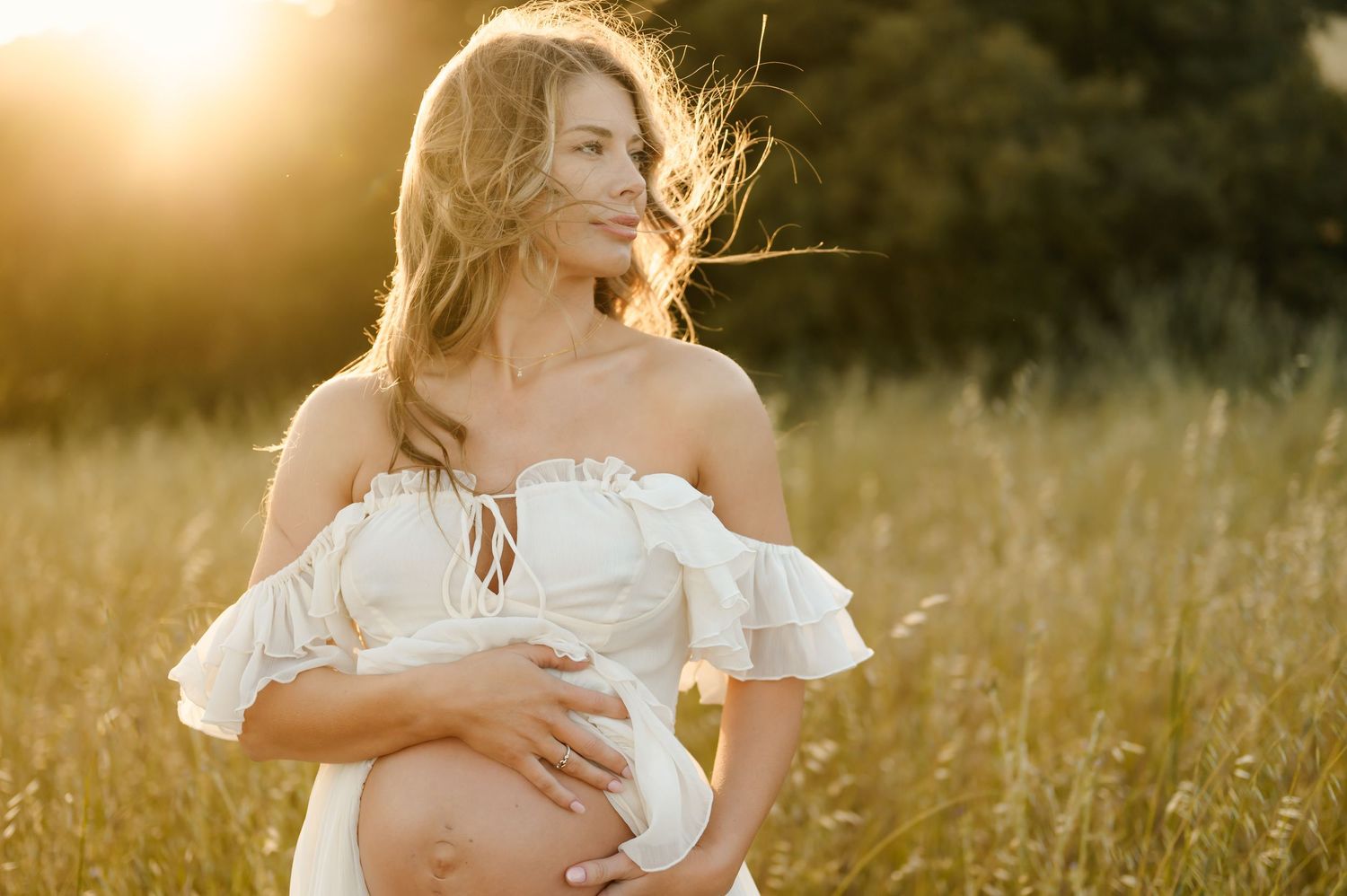 Ojai sunset maternity photoshoot by Ventura maternity photographer of mom holding her bare belly in golden grassy field and white dress