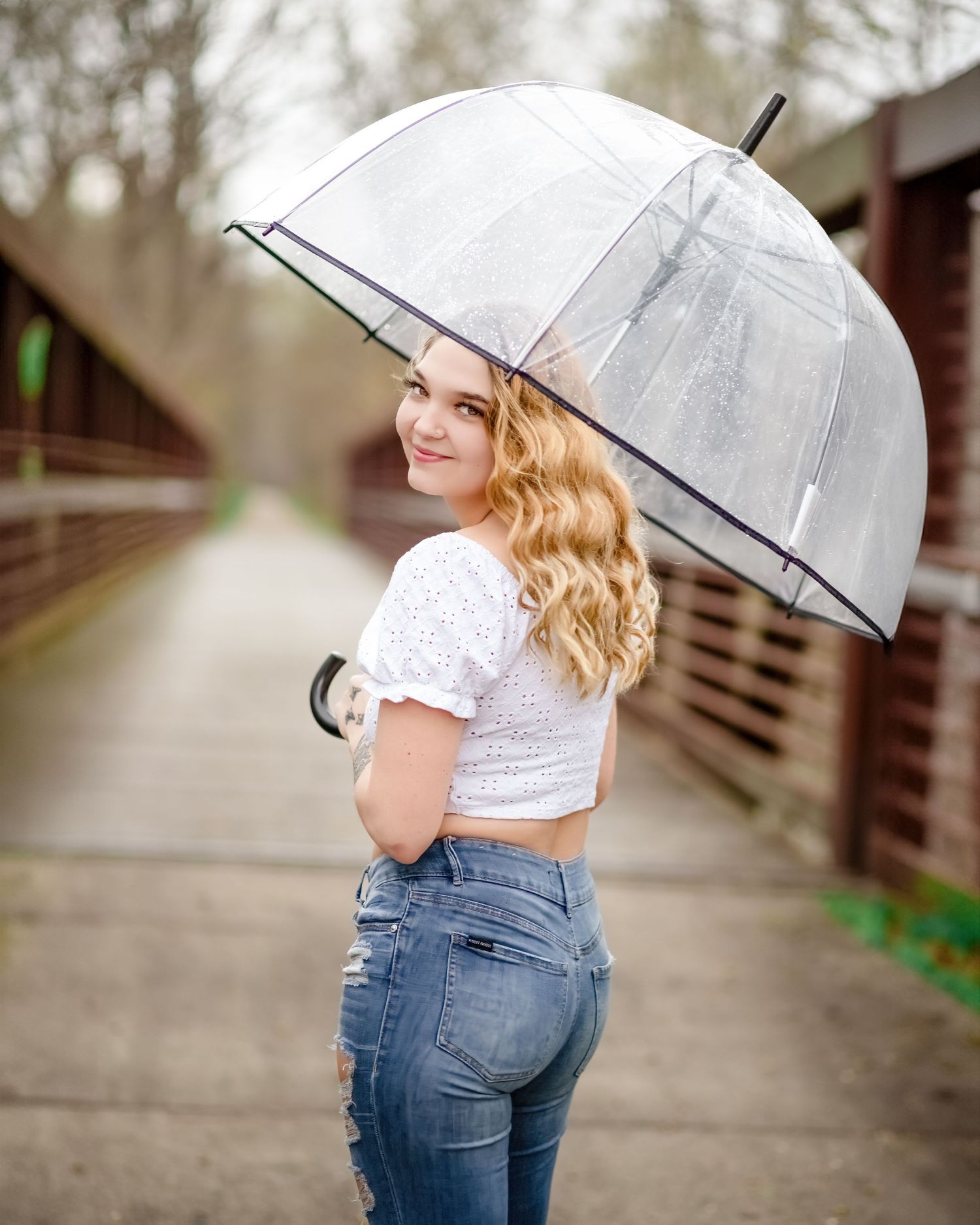 Portrait with clear umbrella on wooden bridge in casual spring outfit.