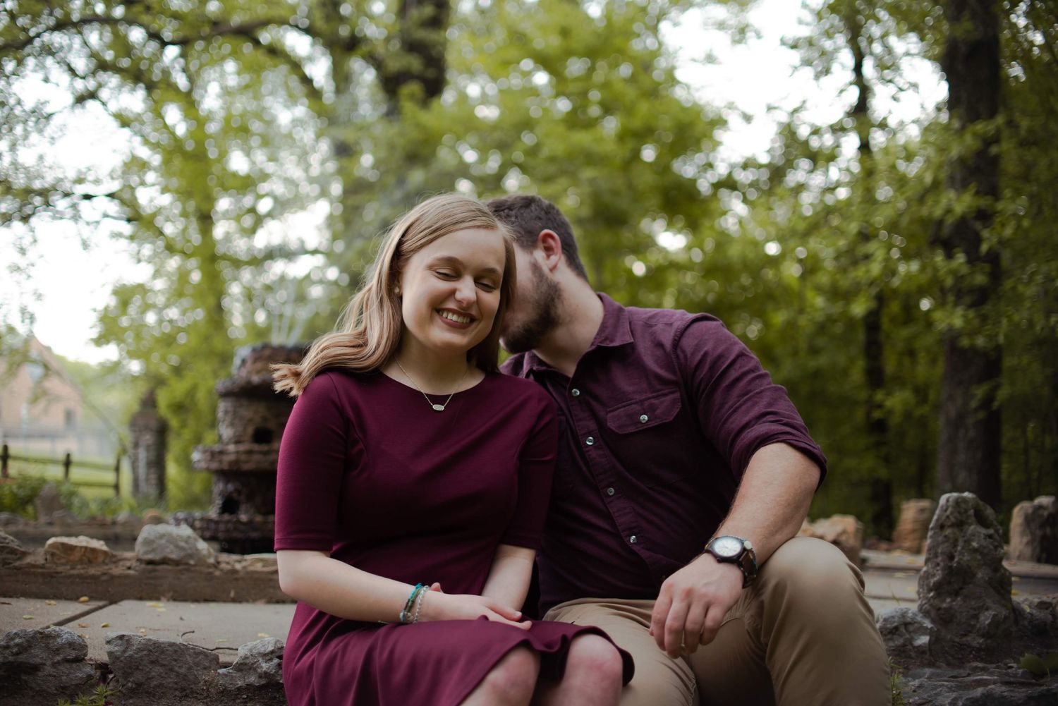 Couple shares an intimate moment while sitting on stone steps in an outdoor garden setting.