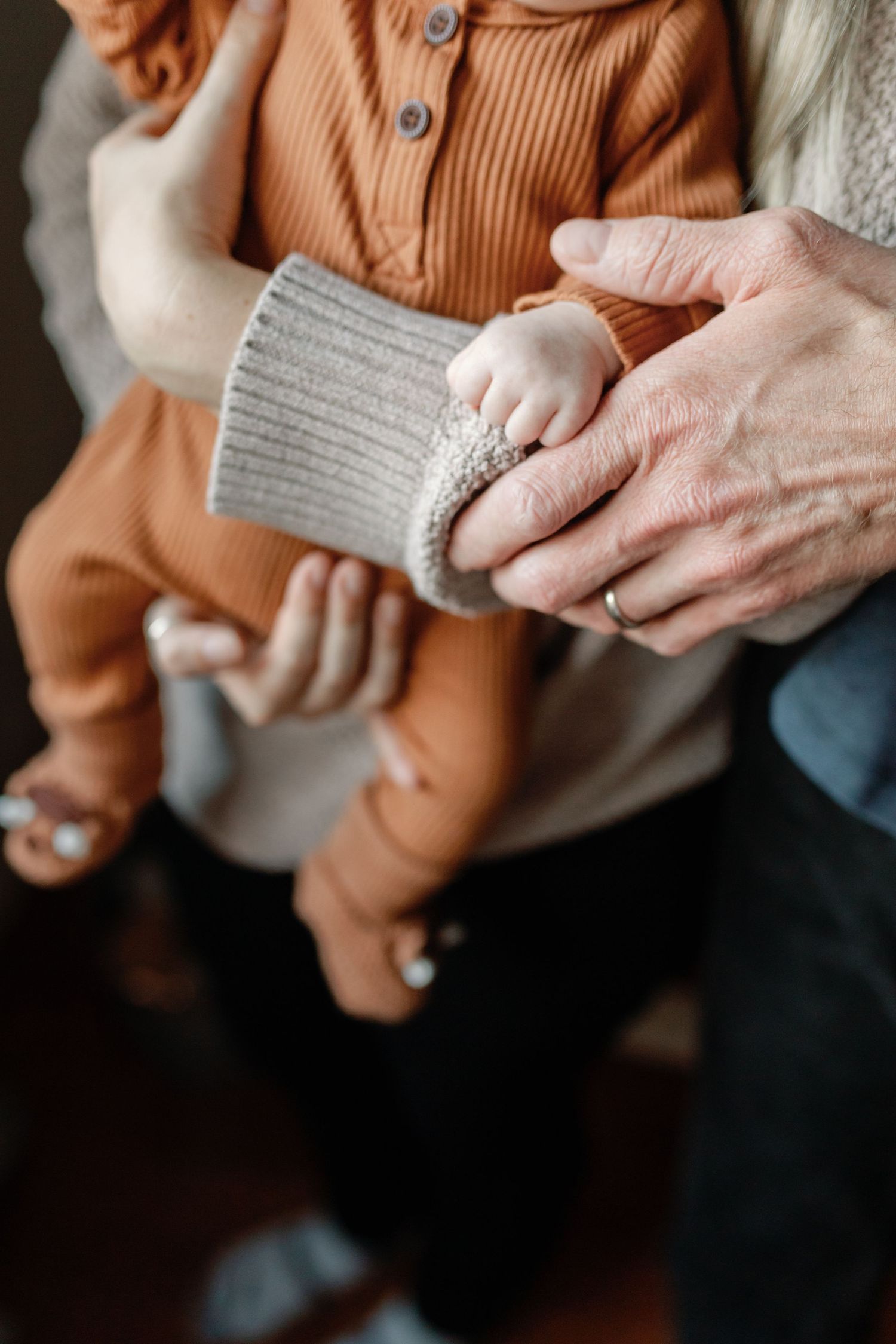Close-up details of hands holding a baby wearing a soft orange knit outfit.