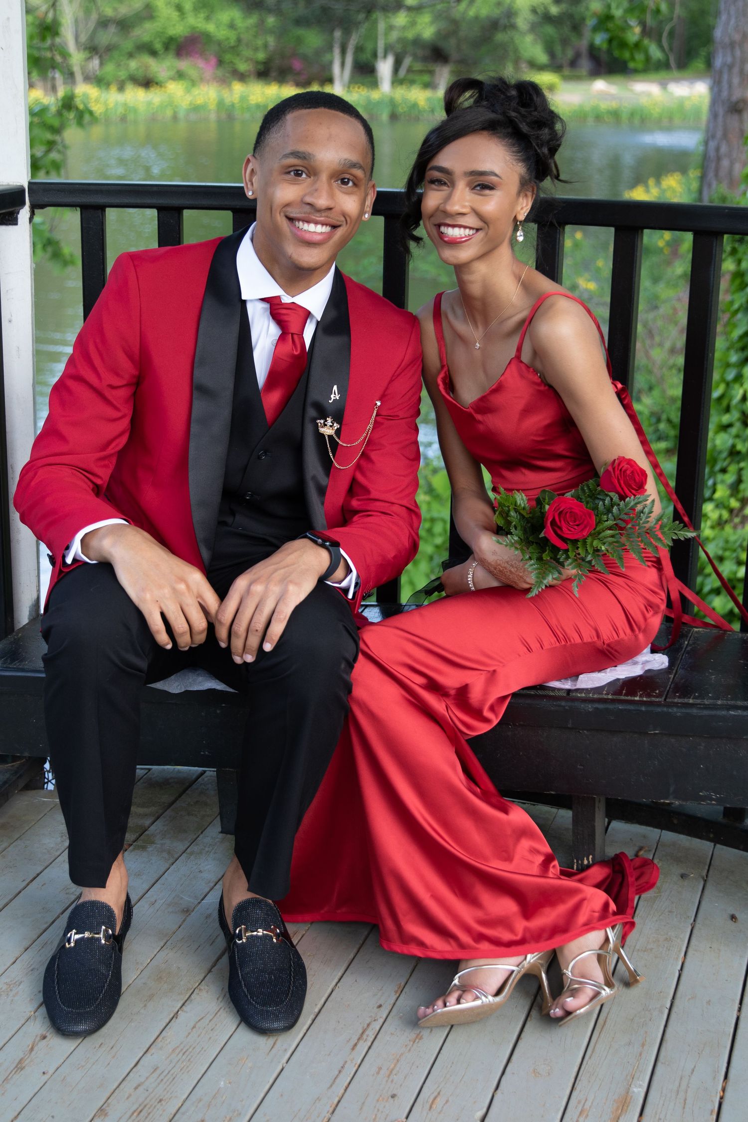 Couple in matching red formal wear sitting together on bench during prom or special event.