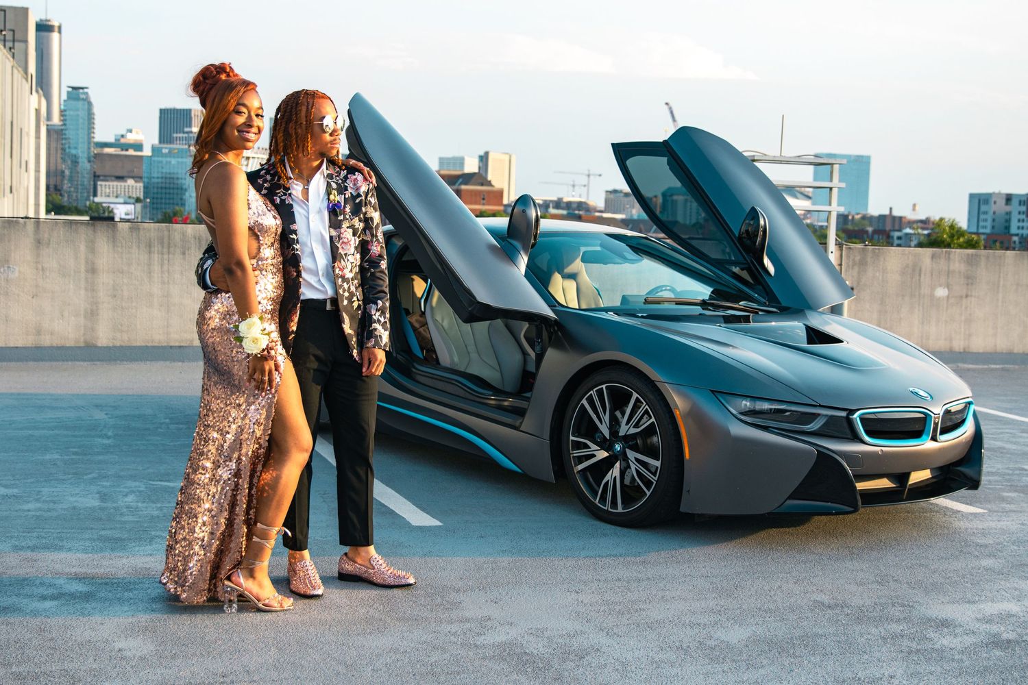 Two people posing with a luxury BMW i8 sports car on an urban rooftop.