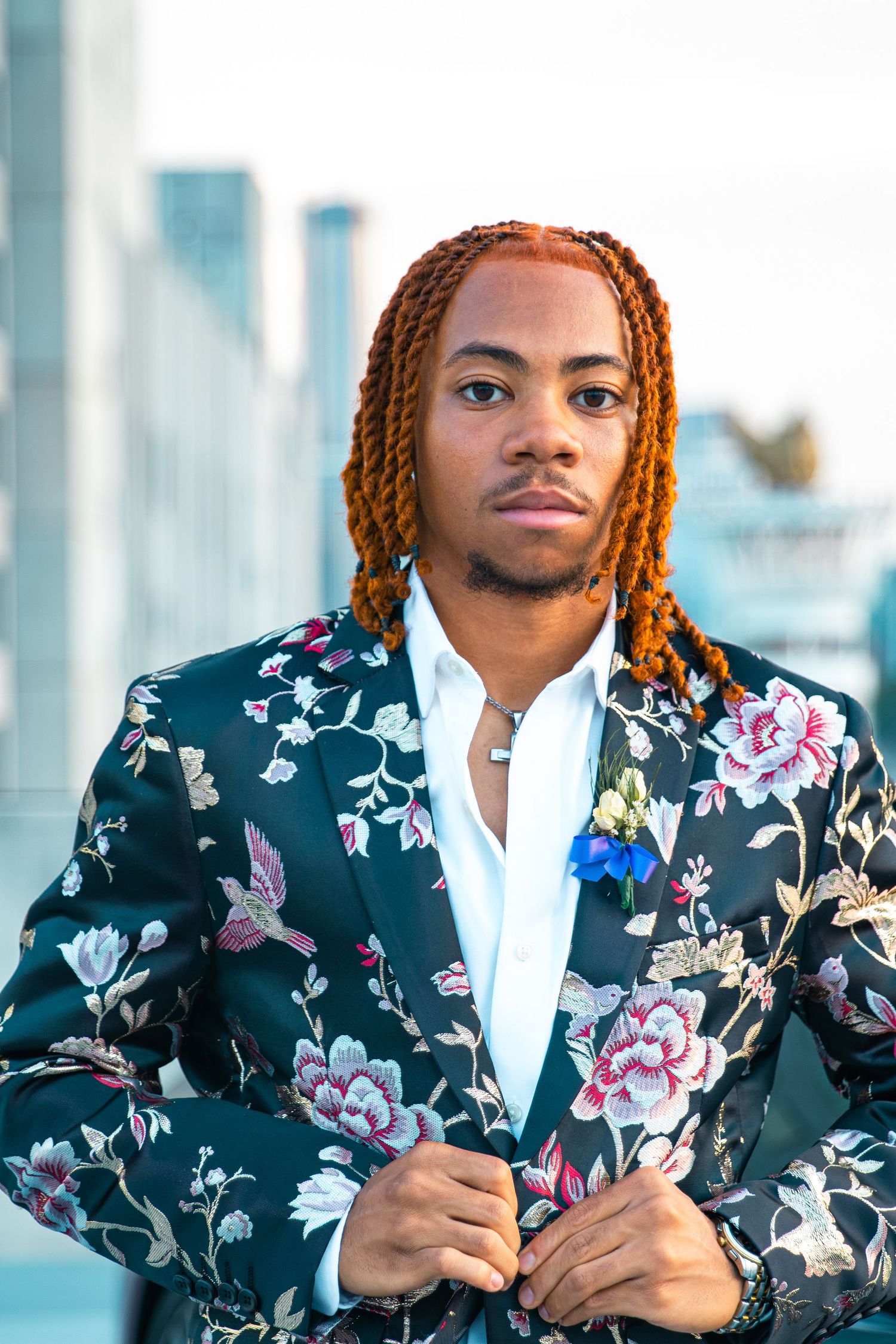 Portrait of person in floral print jacket with braided hair against urban skyline.