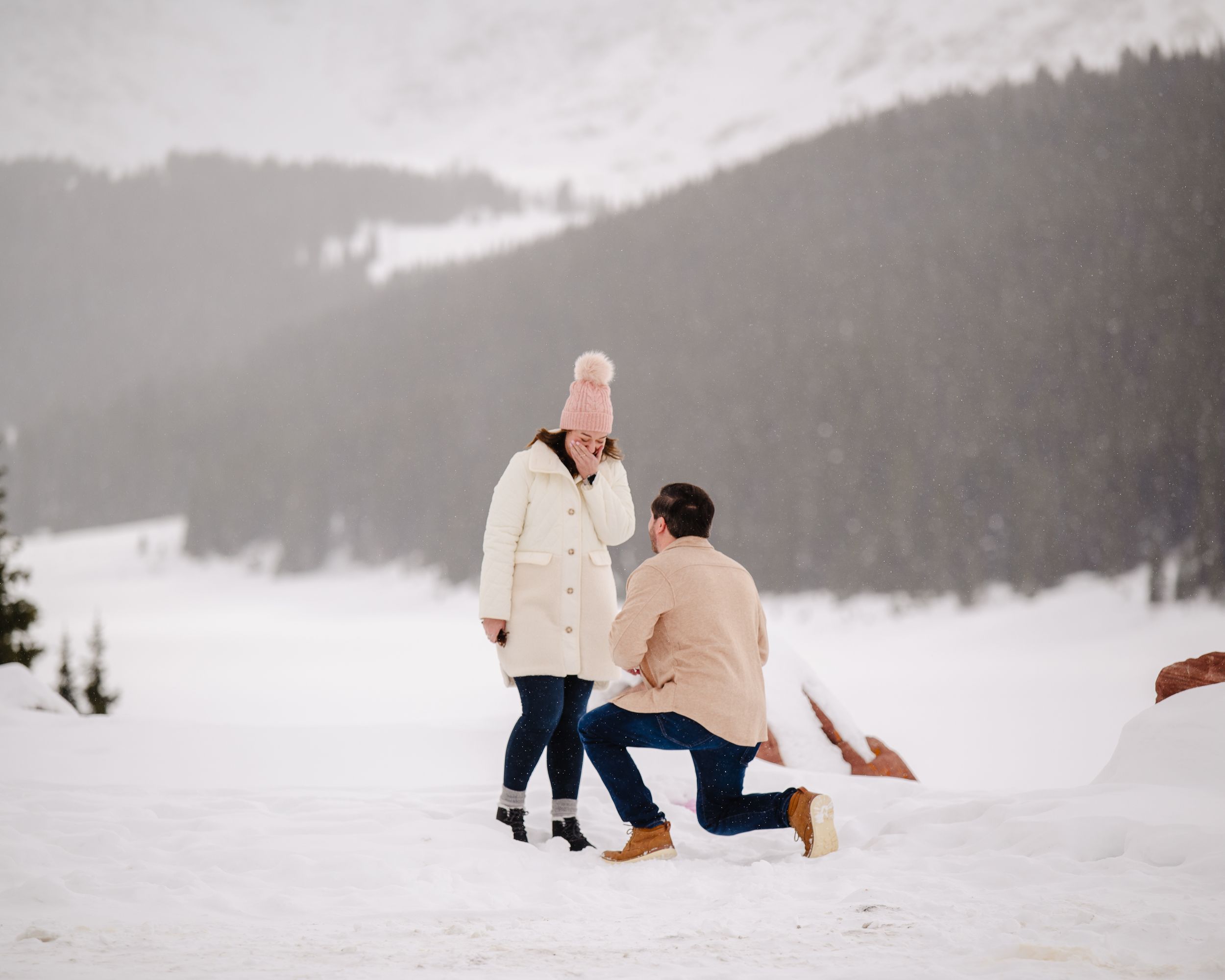 A romantic winter proposal scene unfolds against a snow-covered mountain backdrop.