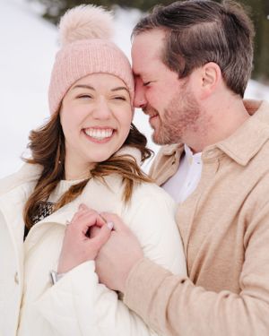 Romantic winter engagement moment captured in the snow with couple laughing.