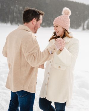 A couple shares a joyful moment together while standing in the snow wearing winter coats.