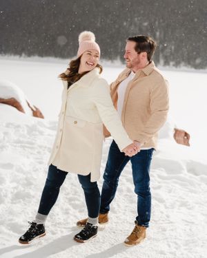 A couple laughs together while enjoying a romantic moment in a snowy mountain landscape.