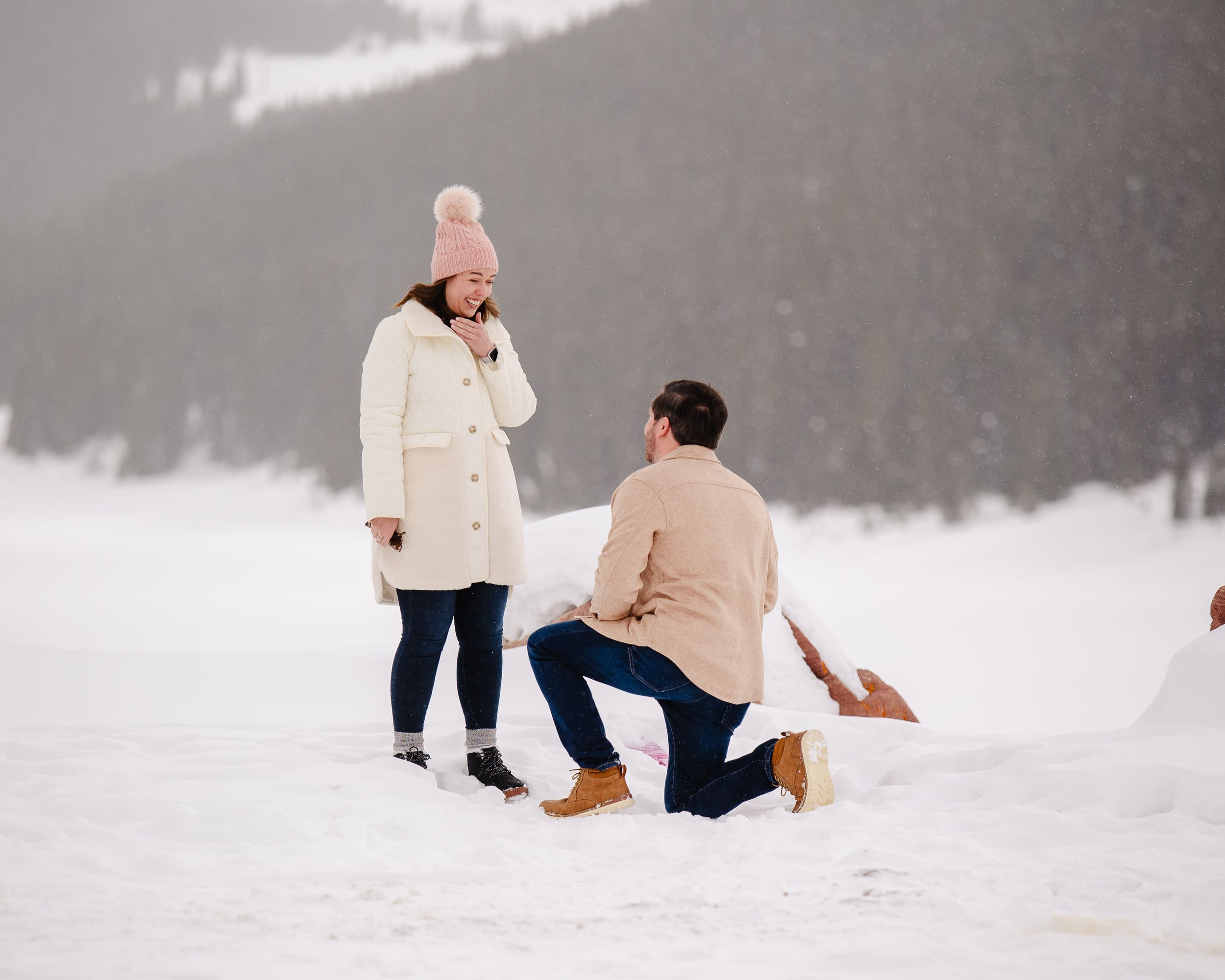 A winter proposal moment captured in the snow with mountains in background.