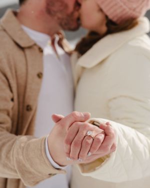 Close-up shot of hands displaying an engagement ring with winter coats in frame.