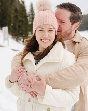 A joyful winter engagement photo with snow-covered mountains in the background.