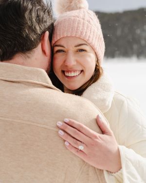A romantic winter engagement moment captured in the snow with warm embraces.