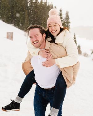 A couple laughing together during a playful piggyback ride in the snow.