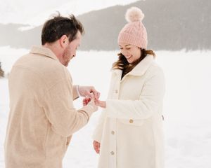 A winter proposal scene with a ring being presented in the snow.