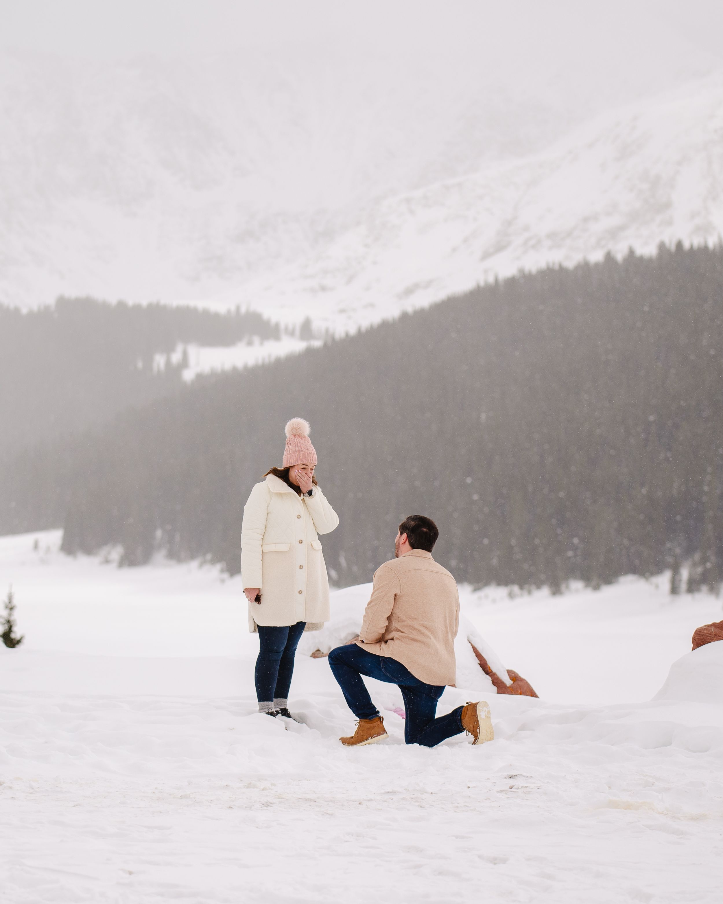 A romantic marriage proposal scene on a snowy winter mountain landscape.