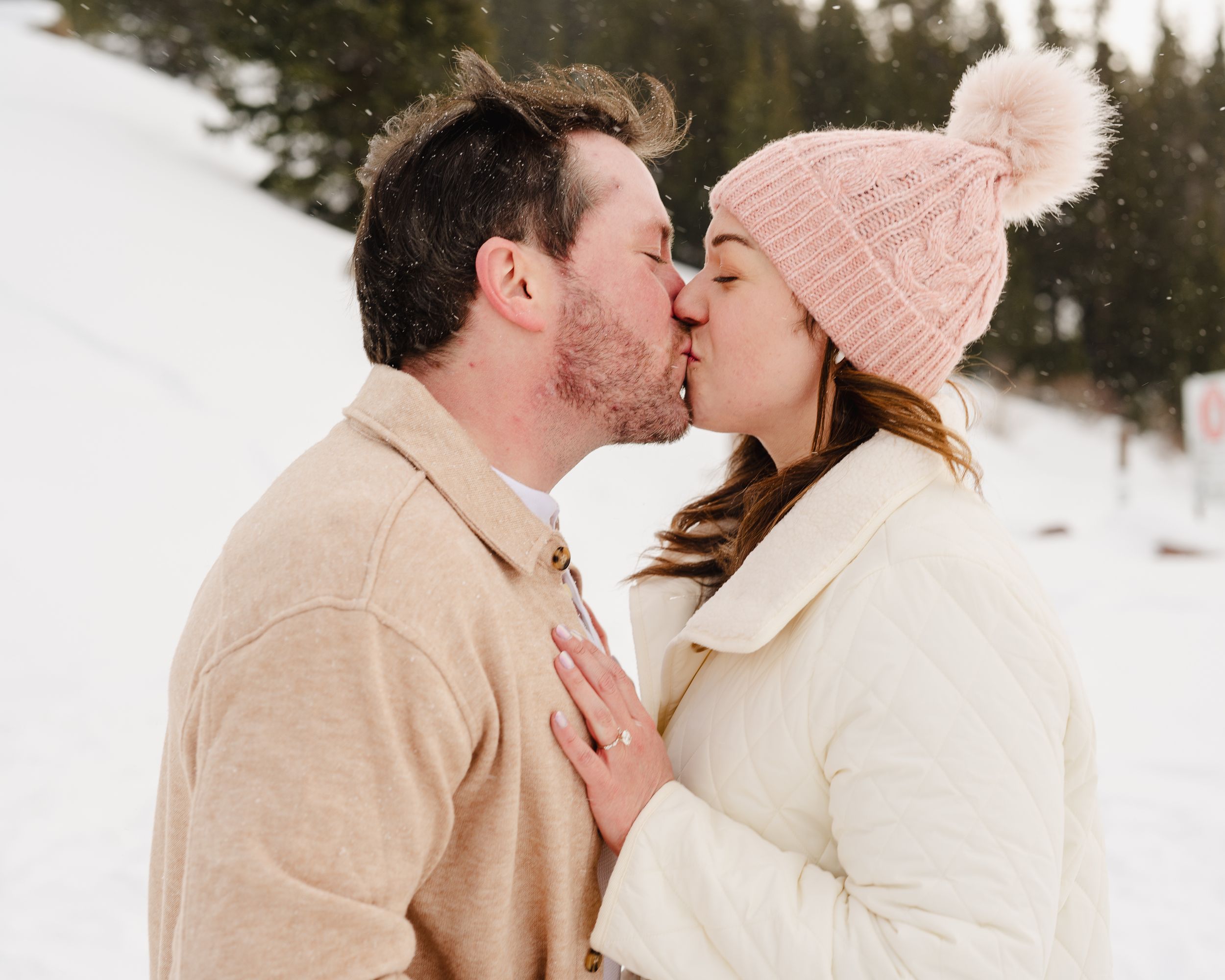 A romantic kiss shared between a couple after their snowy engagement.