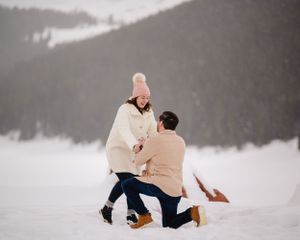A romantic winter proposal scene unfolds against a snowy mountain backdrop.