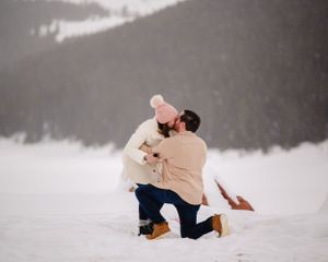 A magical moment captured in the snow as someone proposes in front of mountain scenery.