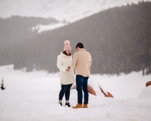 Two people share an intimate moment in matching beige outfits against a snowy mountain landscape.