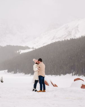 A couple embraces in winter attire against a snow-covered mountain vista.
